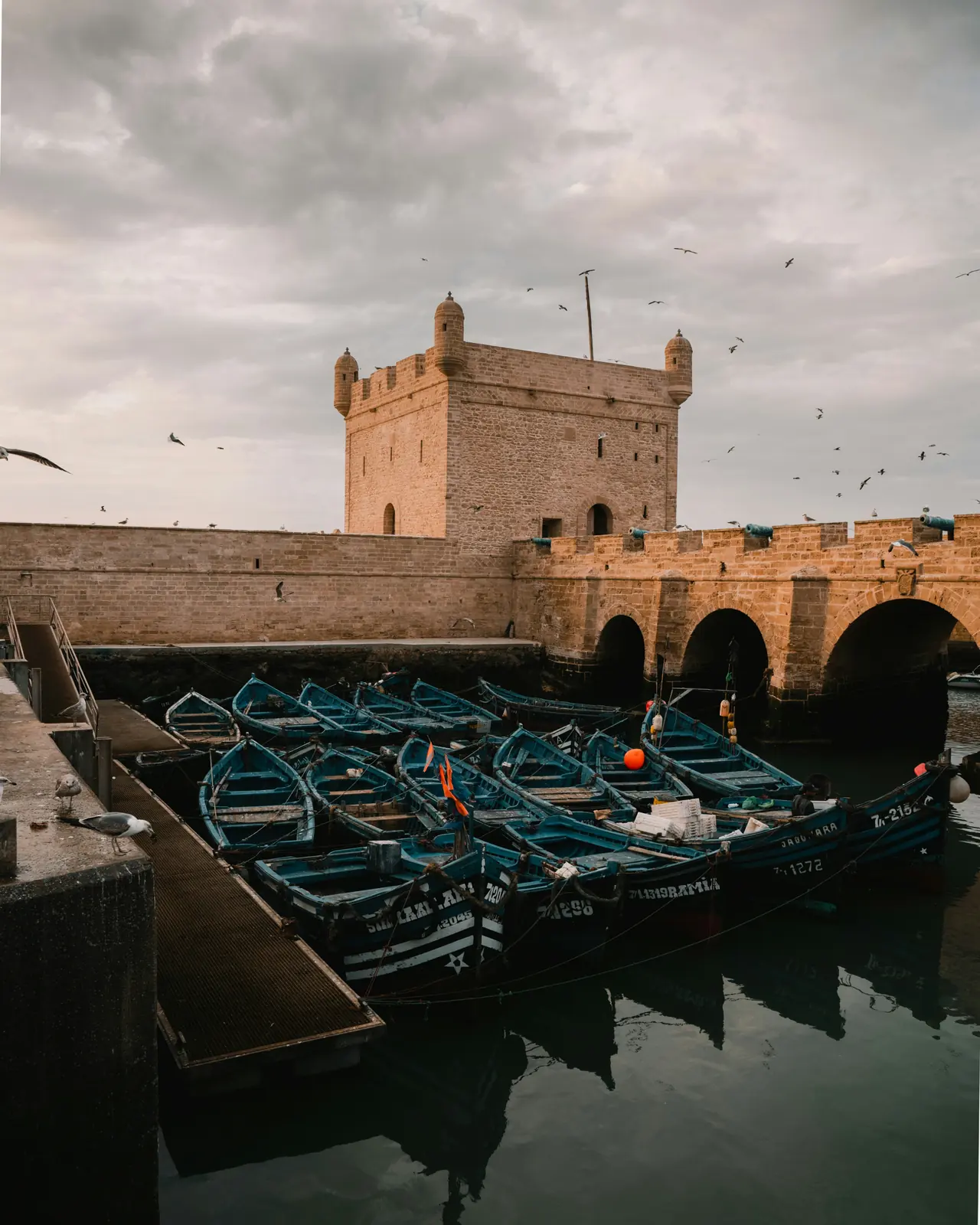 Barques de pêche bleues amarrées devant le bastion du port d'Essaouira