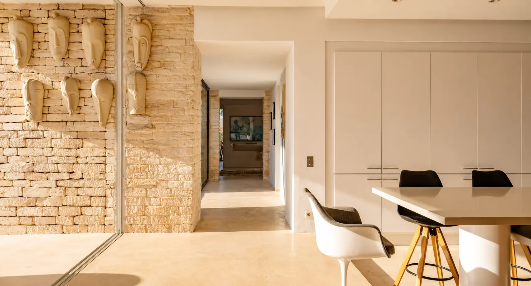 Mur en pierre sèche orné de masques africains sculptés, près de la cuisine de la Villa Nausikaa