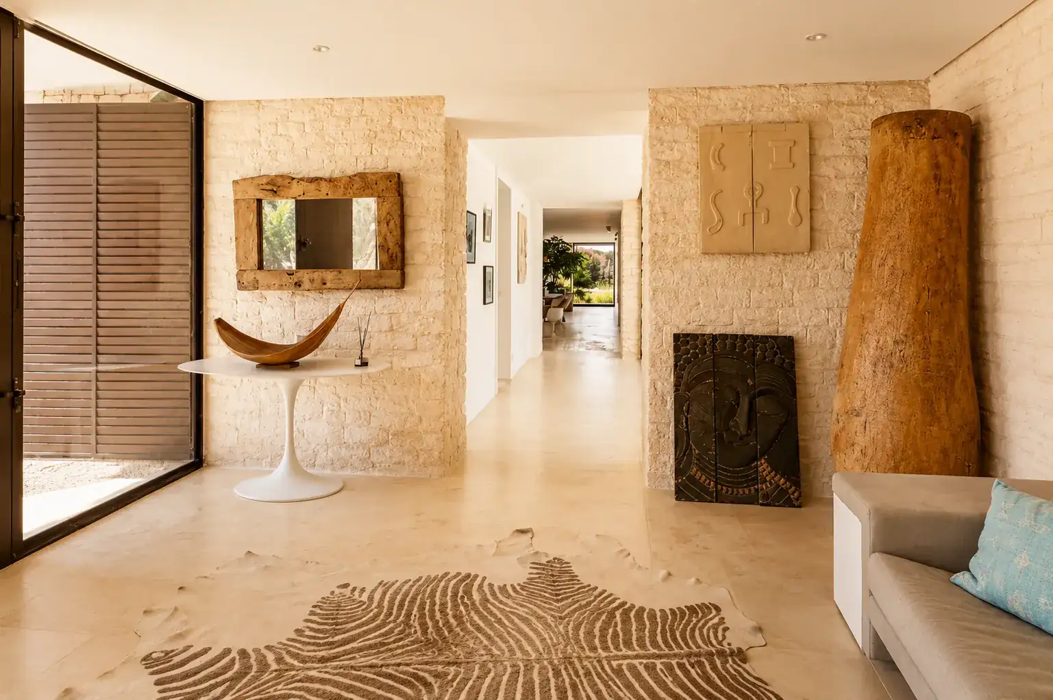 Galerie d'entrée de la Villa Nausikaa : murs en pierre sèche, miroir en bois flotté et pièces d'art