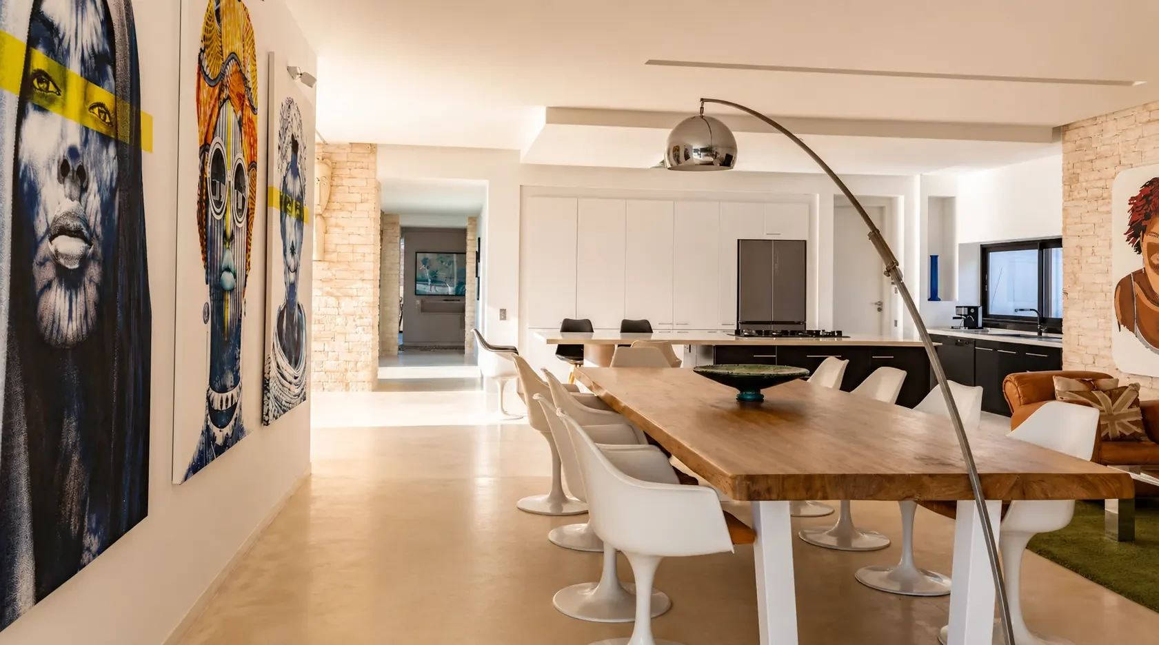 Table d'hôtes en bois brut, chaises Tulip blanches et mur d'œuvres contemporaines à la Villa Nausikaa