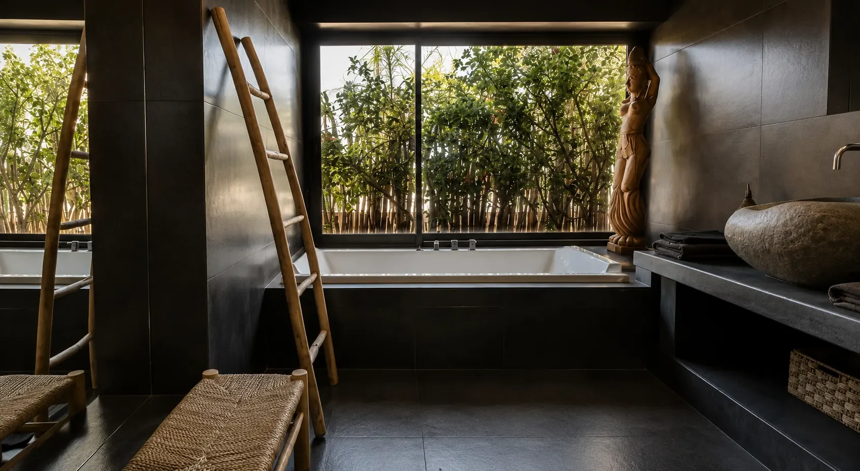 Baignoire encastrée sous la fenêtre dans une salle de bain en pierre sombre de la Villa Nausikaa