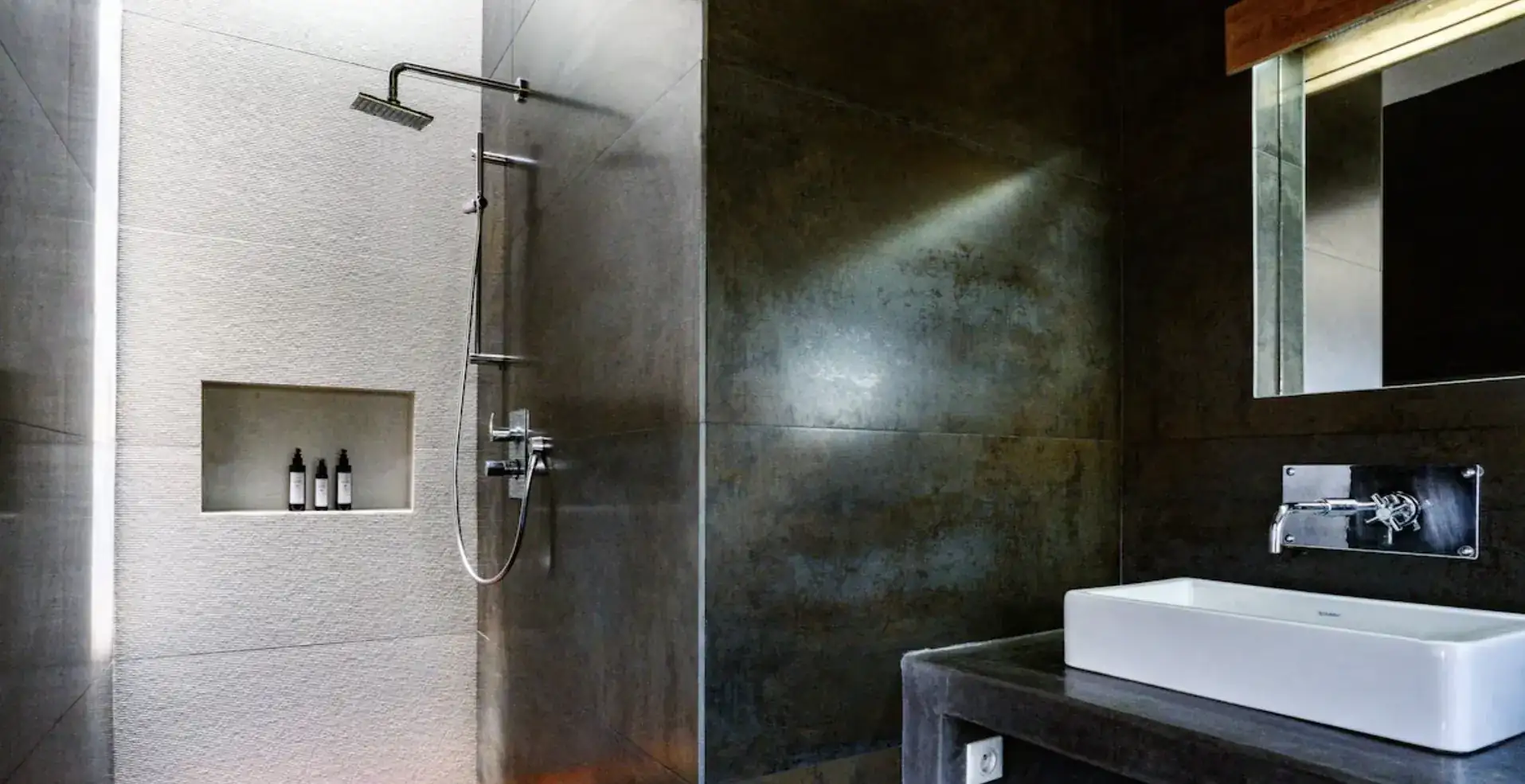 Douche à l'italienne en pierre claire et parois sombres dans la suite parentale de la Villa Nausikaa